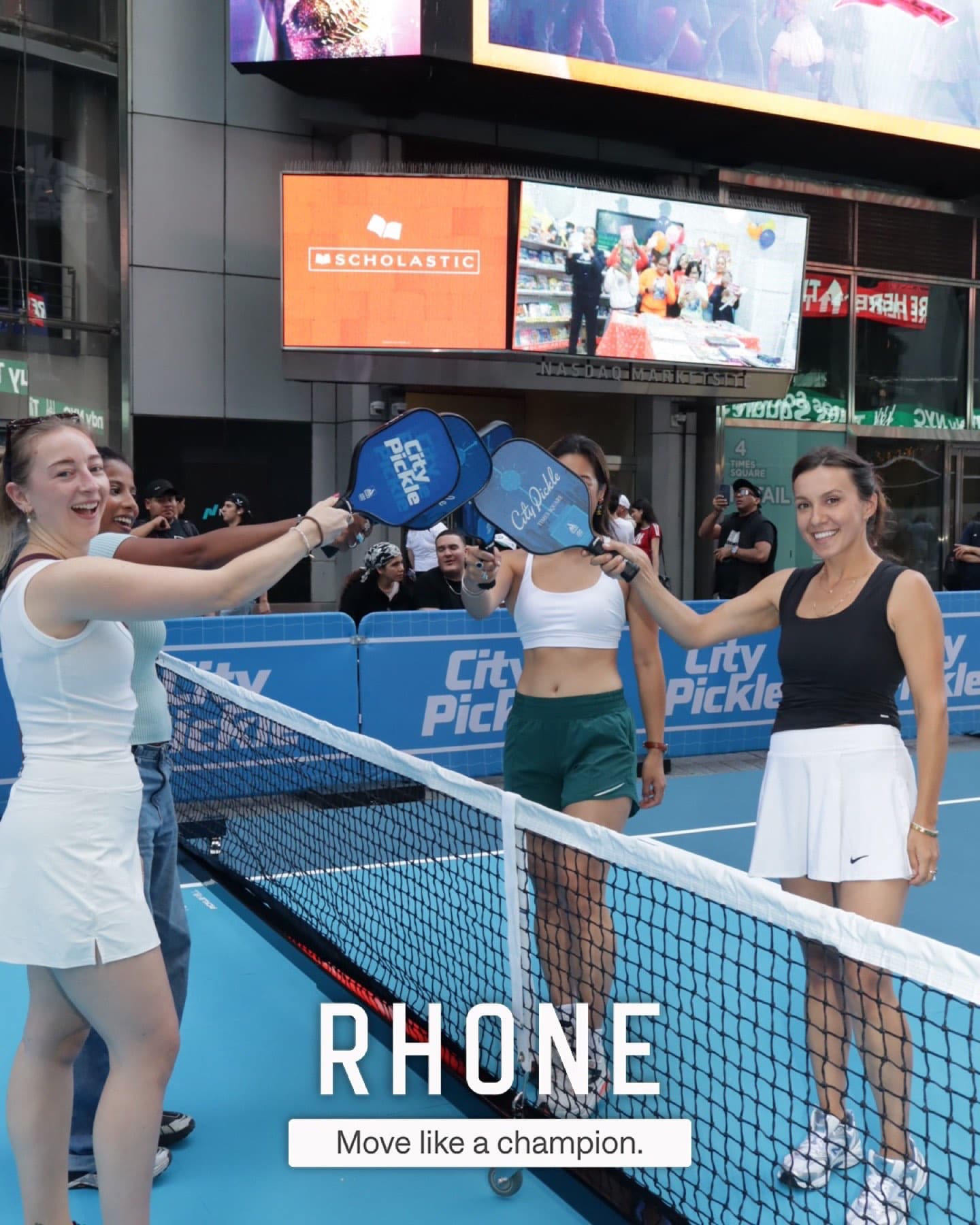 Guests reach across the pickleball net holding City Pickle paddles under the Times Square billboards.