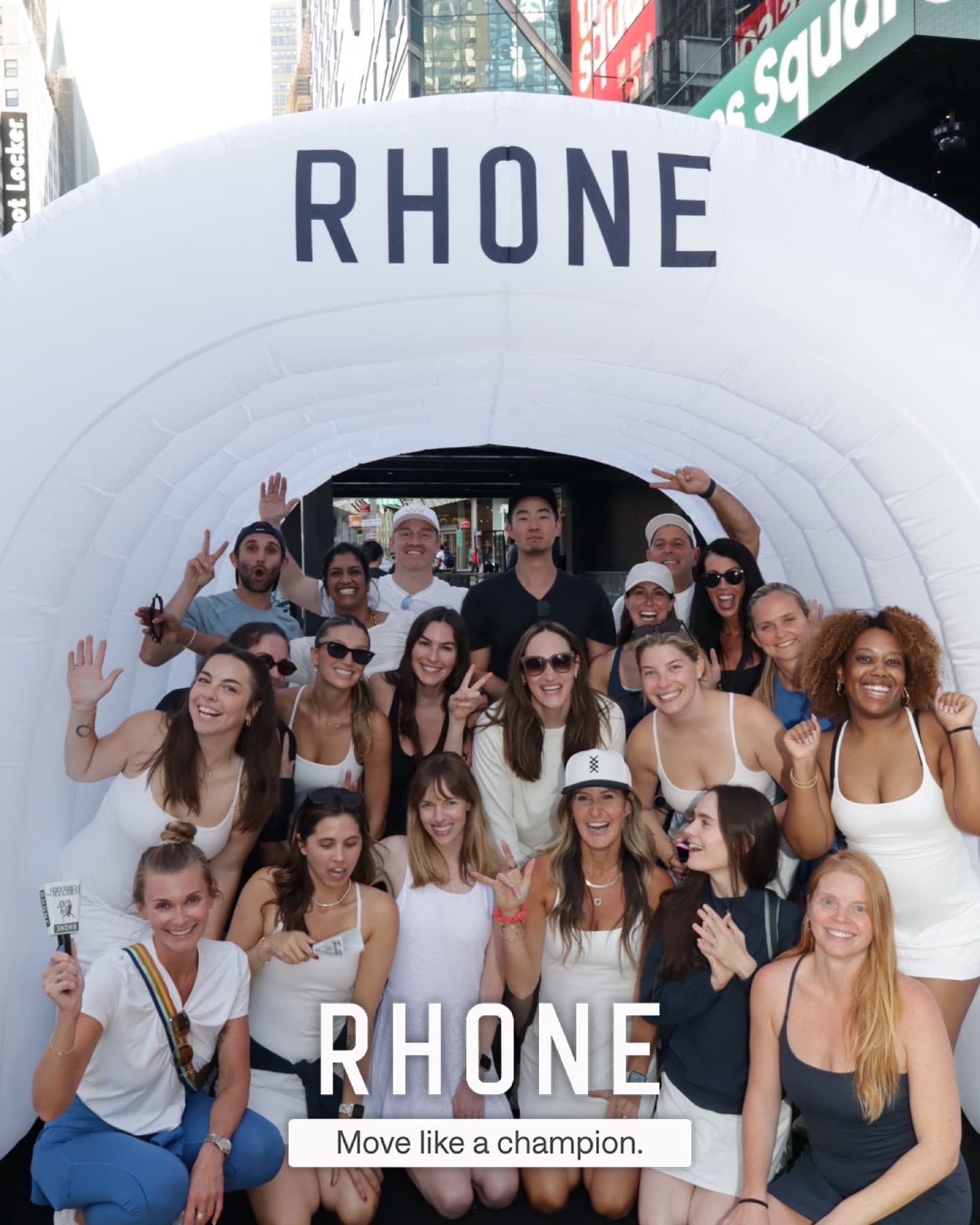 A large group poses inside the Rhone-branded inflatable tunnel in Times Square, with the delivered photo's "RHONE / Move like a champion." overlay visible.