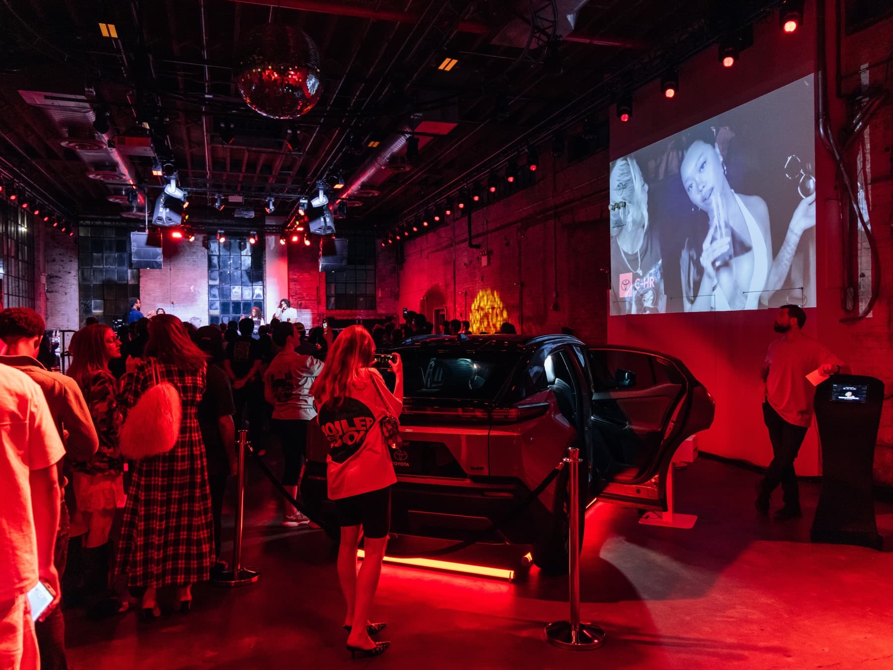 The Toyota C-HR on the party floor at 99 Scott Ave, Brooklyn, guests seated inside as the crowd gathers around it.