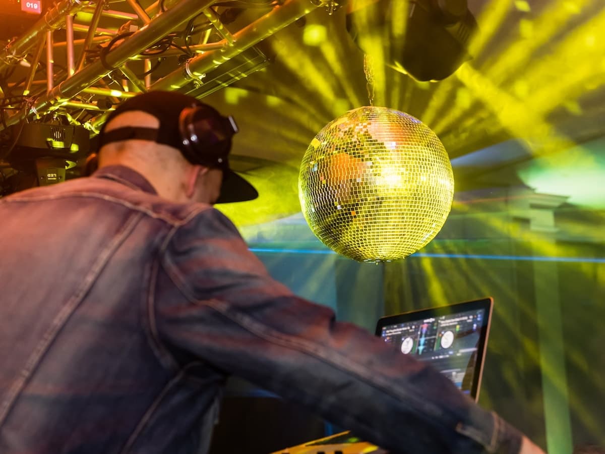 DJ performing beside a gold mirror ball under warm show lighting.